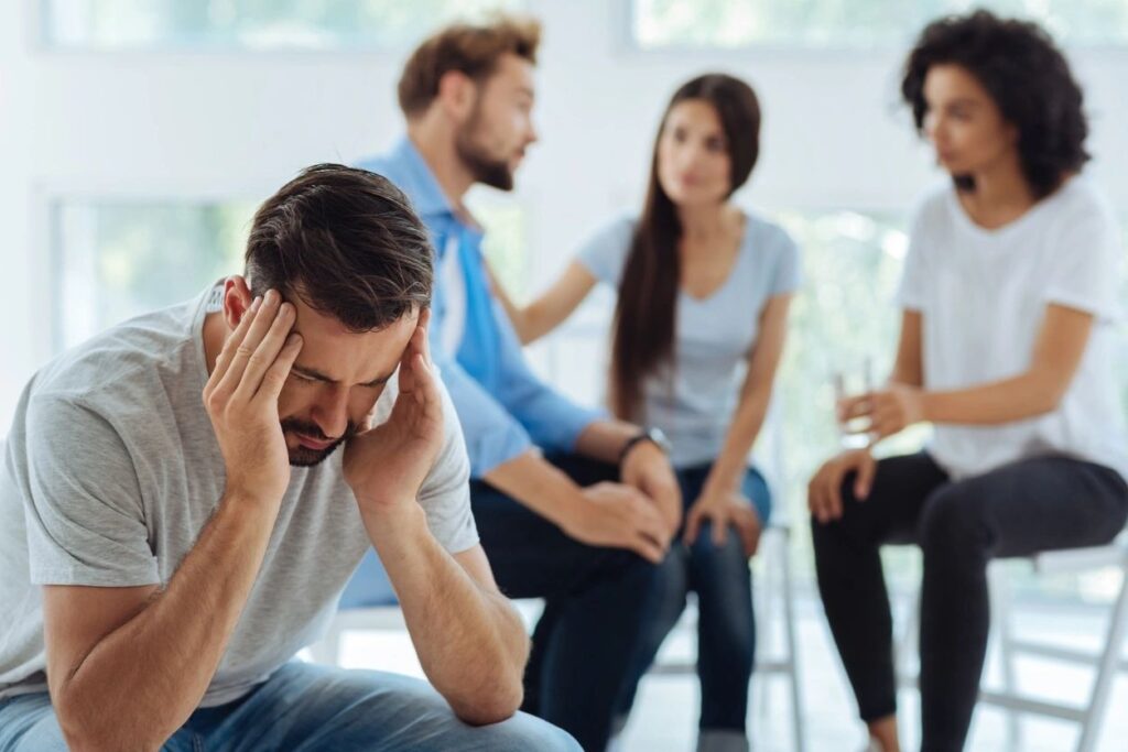 A man holding his head while other people talk